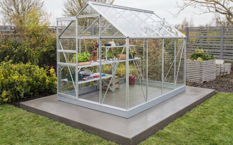 Silver Vitavia Venus 5000 greenhouse fitted on a freshly poured concrete pad in a UK back garden