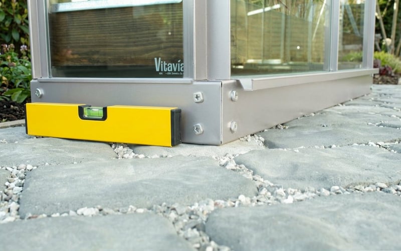 Vitavia aluminium greenhouse base frame on paving slabs with spirit level checking for level